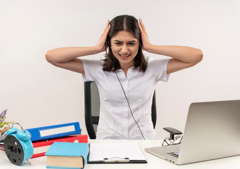 young-girl-white-shirt-headphones-looking-tired-overworked-sitting-table-with-folders-laptop-white-wall_141793-52675